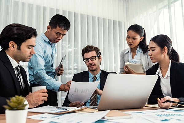a group of bank workers sitting around a table looking at a graph on a piece of paper.