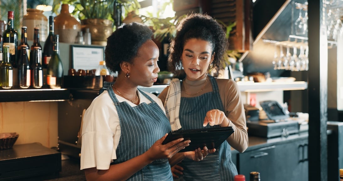 female servers looking at an iPad behind the bar