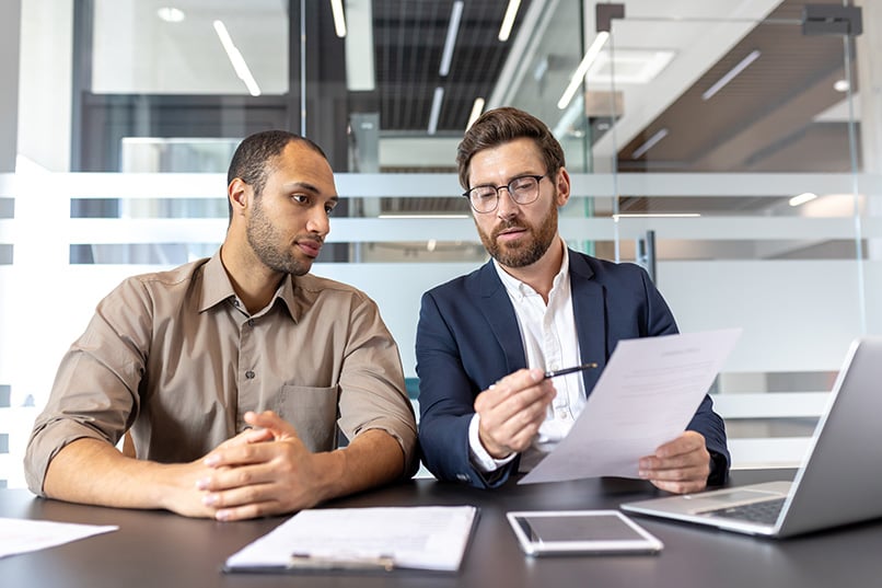 two business men looking over a sheet of paper at a table.