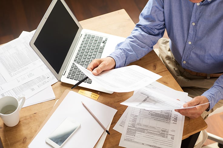 a man with a stack of papers on his desk filling out tax forms with his laptop