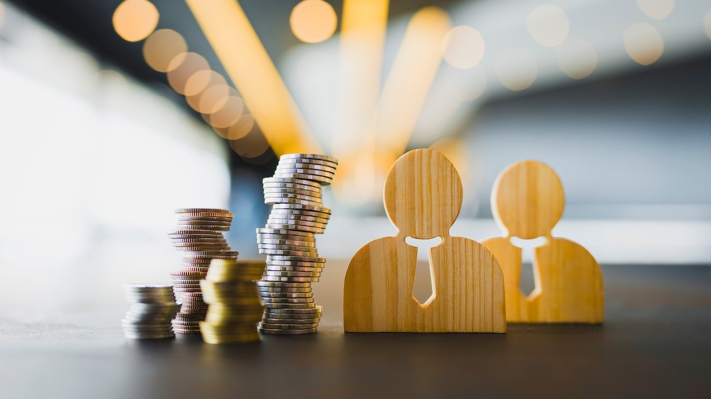 two wooden business man cutouts next to stacks of coins