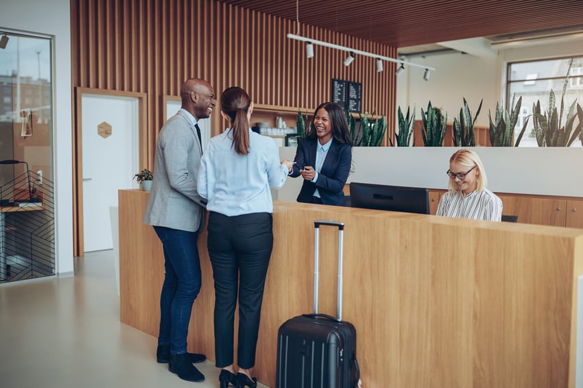 two business people checking in at the hotel front desk with a smiling desk agent.