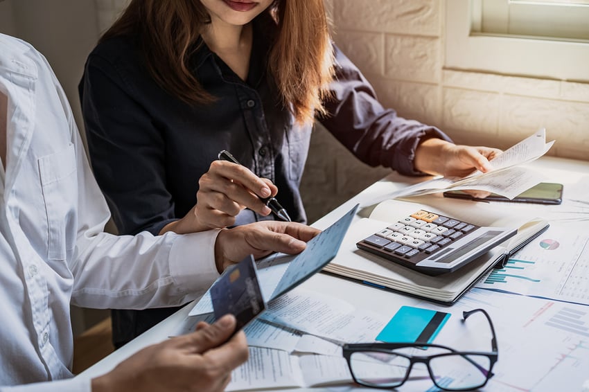 a business man and woman sitting at a desk looking at a check and calculating numbers.