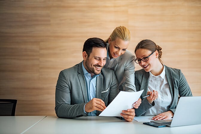 a corporate woman explains a document to a corporate man and woman.