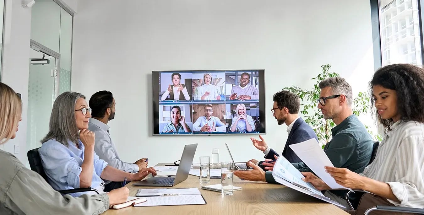 a group of corporate workers have a meeting with some virtually attending.