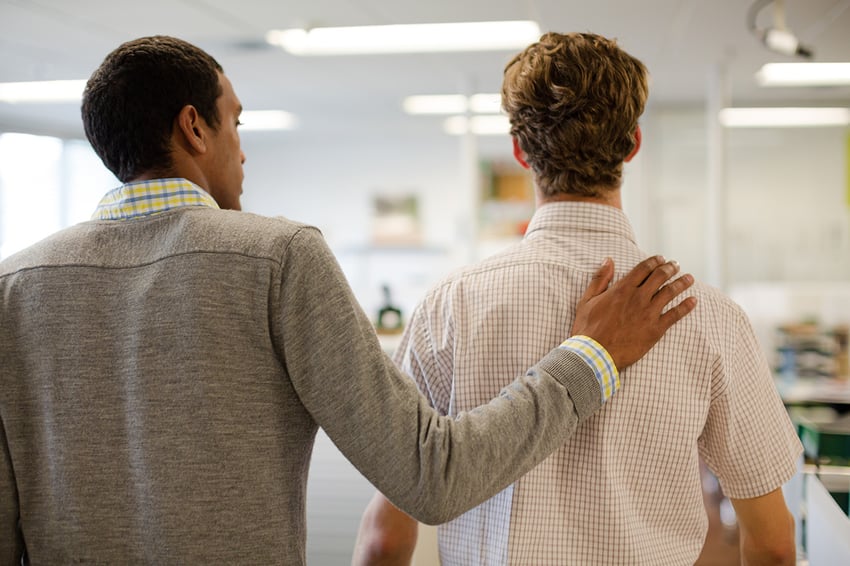 a man comforts his coworker in an office.