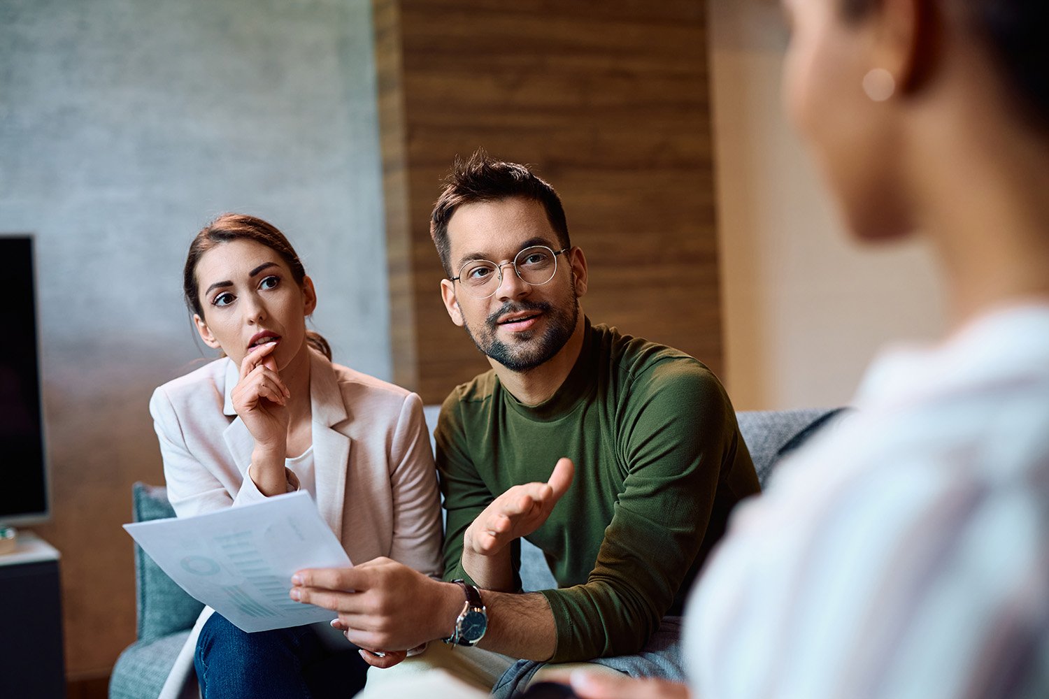 a young couple sitting on a couch talk with a female about insurance plans.