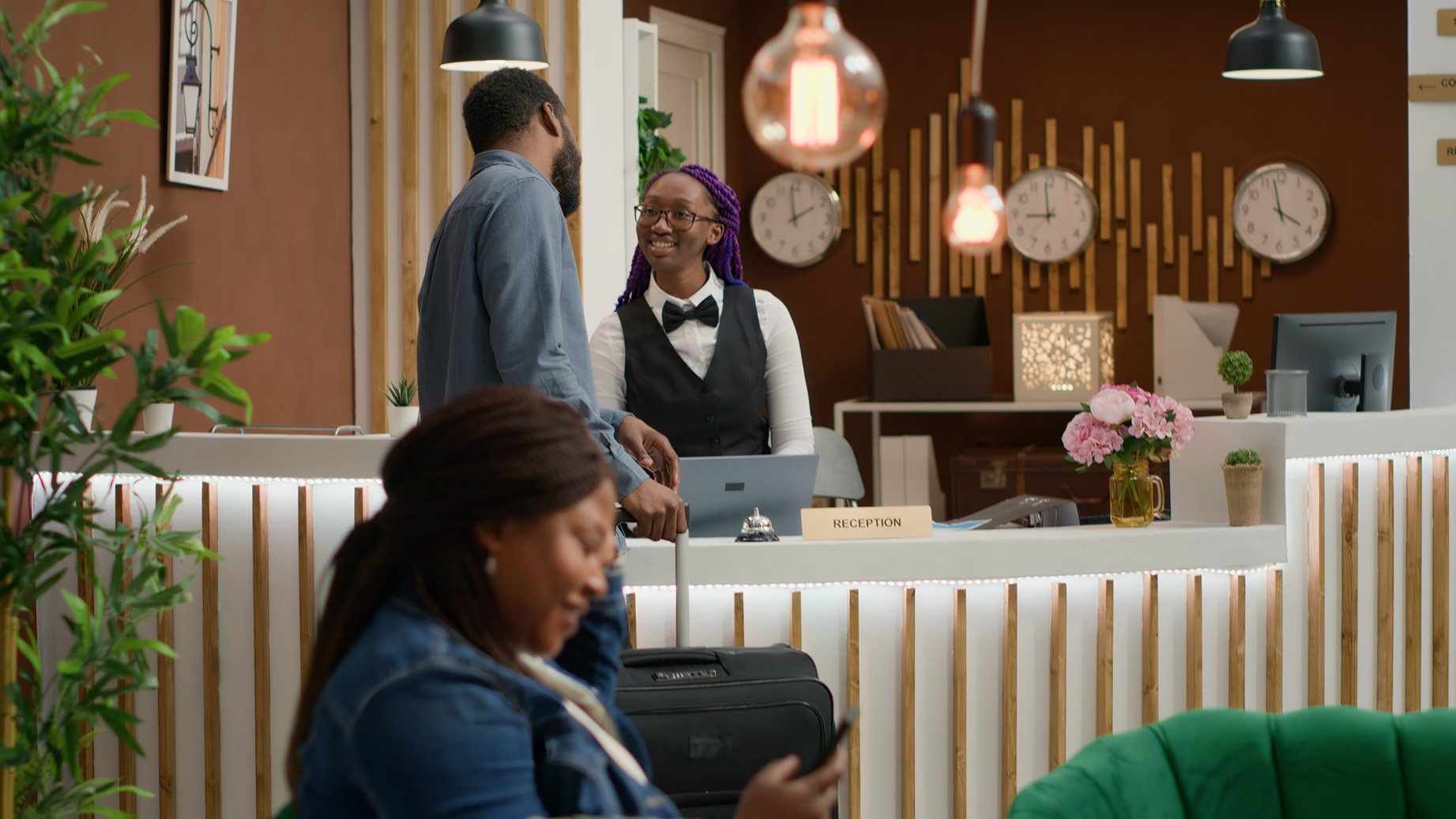 a female hotel worker checks in a guest at the reception desk.
