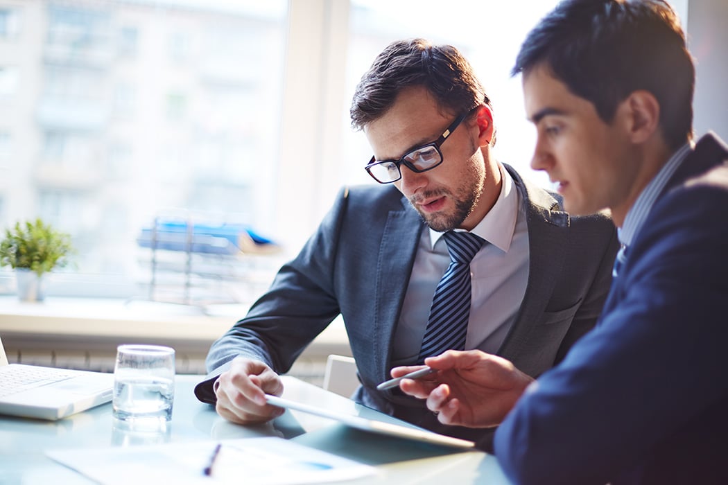 two male bankers look at a piece of paper together.