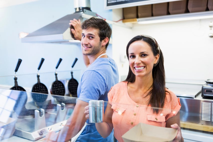 two-people-behind-the-counter-at-a-cafe-smile-for-a-photo