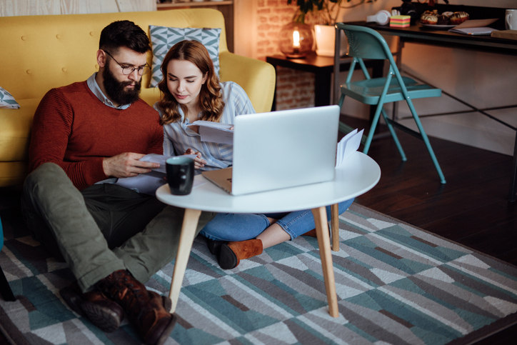 two people sit on the ground looking at a computer and pieces of paper