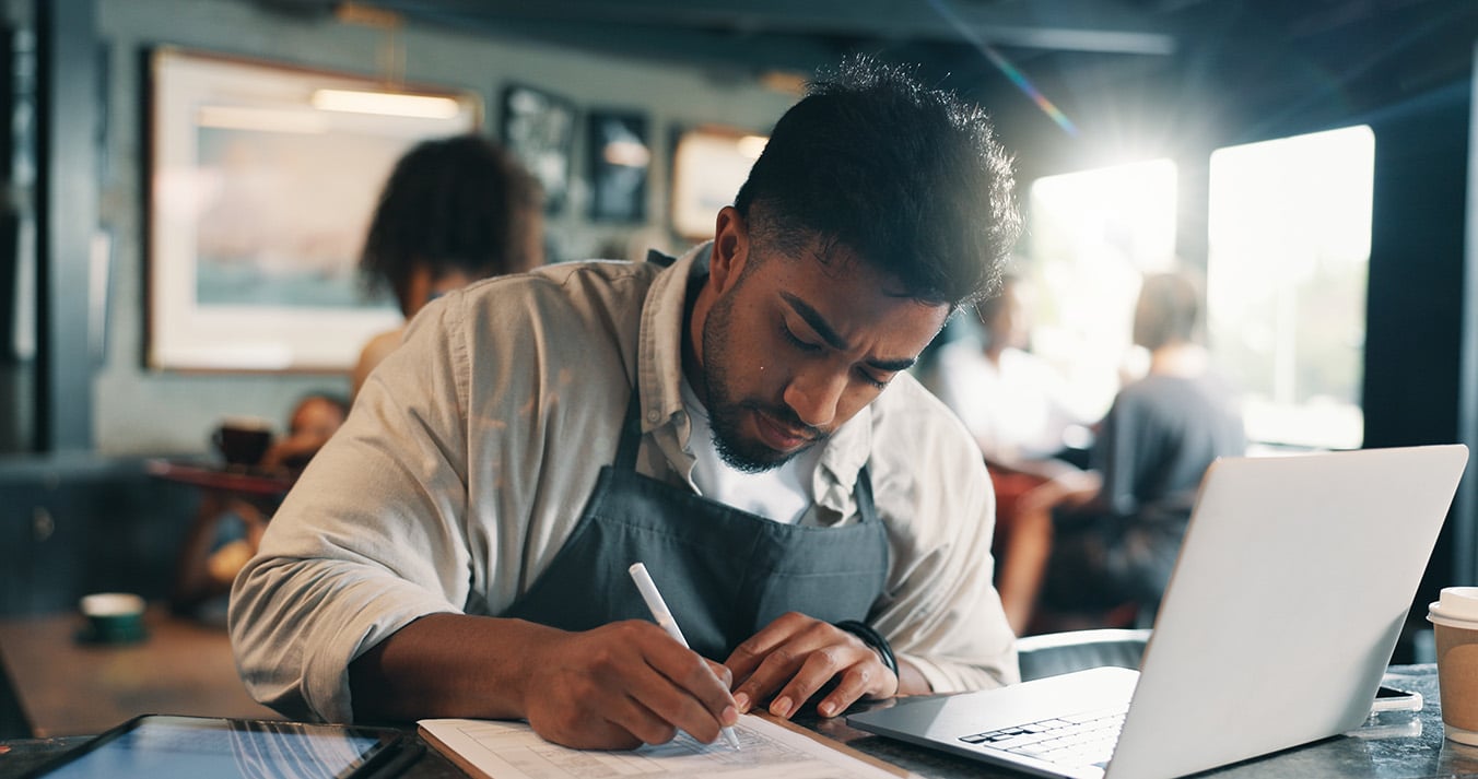 a man with an apron on at a restaurant fills out his taxes.