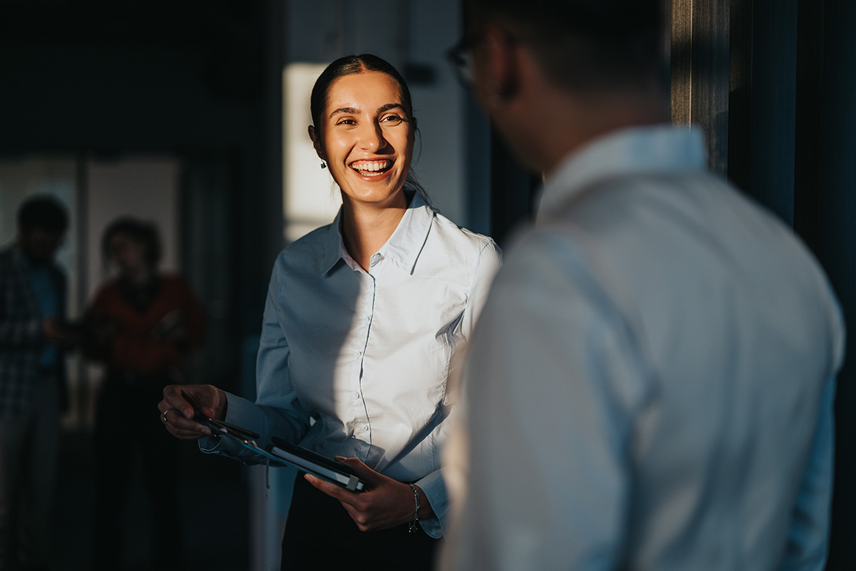 a male and female employee speak and smile together in an office.