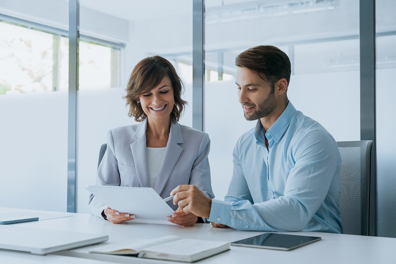 Latin woman accountant analyst holding document working with European client man doing trade market financial data base bank report. Businesswoman and businessman reading paperwork contract in office.