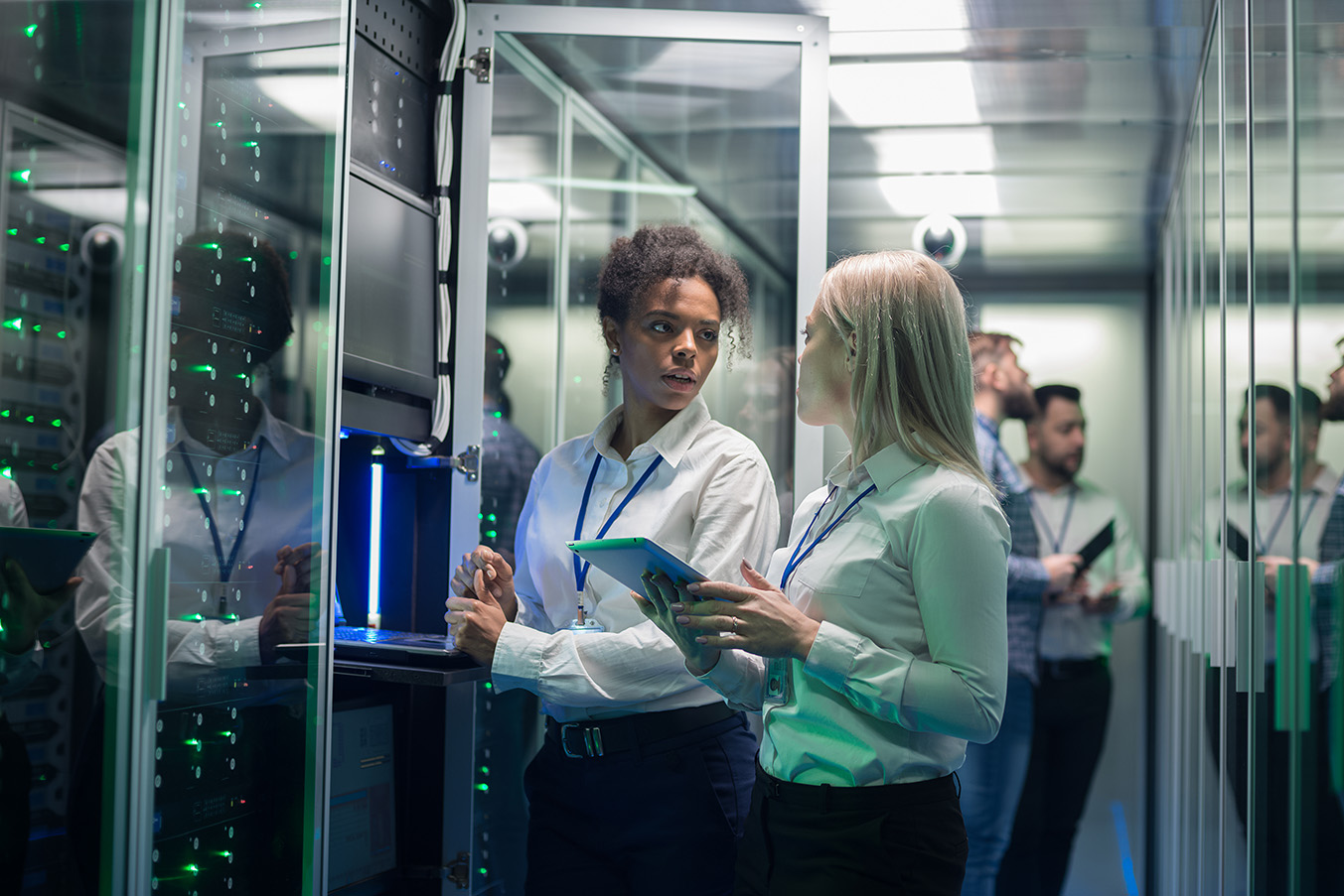 two-women-working-in-a-data-center-stand-and-talk-near-a-server-rack