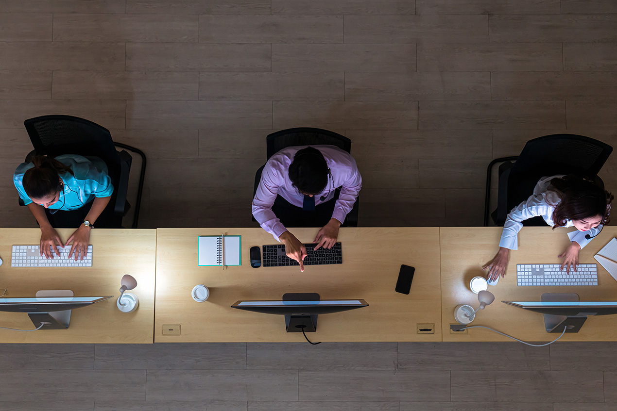 three workers all working at their computers while the one in the middle points at his screen.