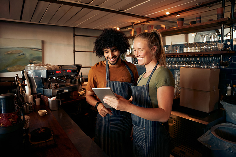 two-service-workers-standing-behind-a-bar-smiling-while-looking-at-an-ipad