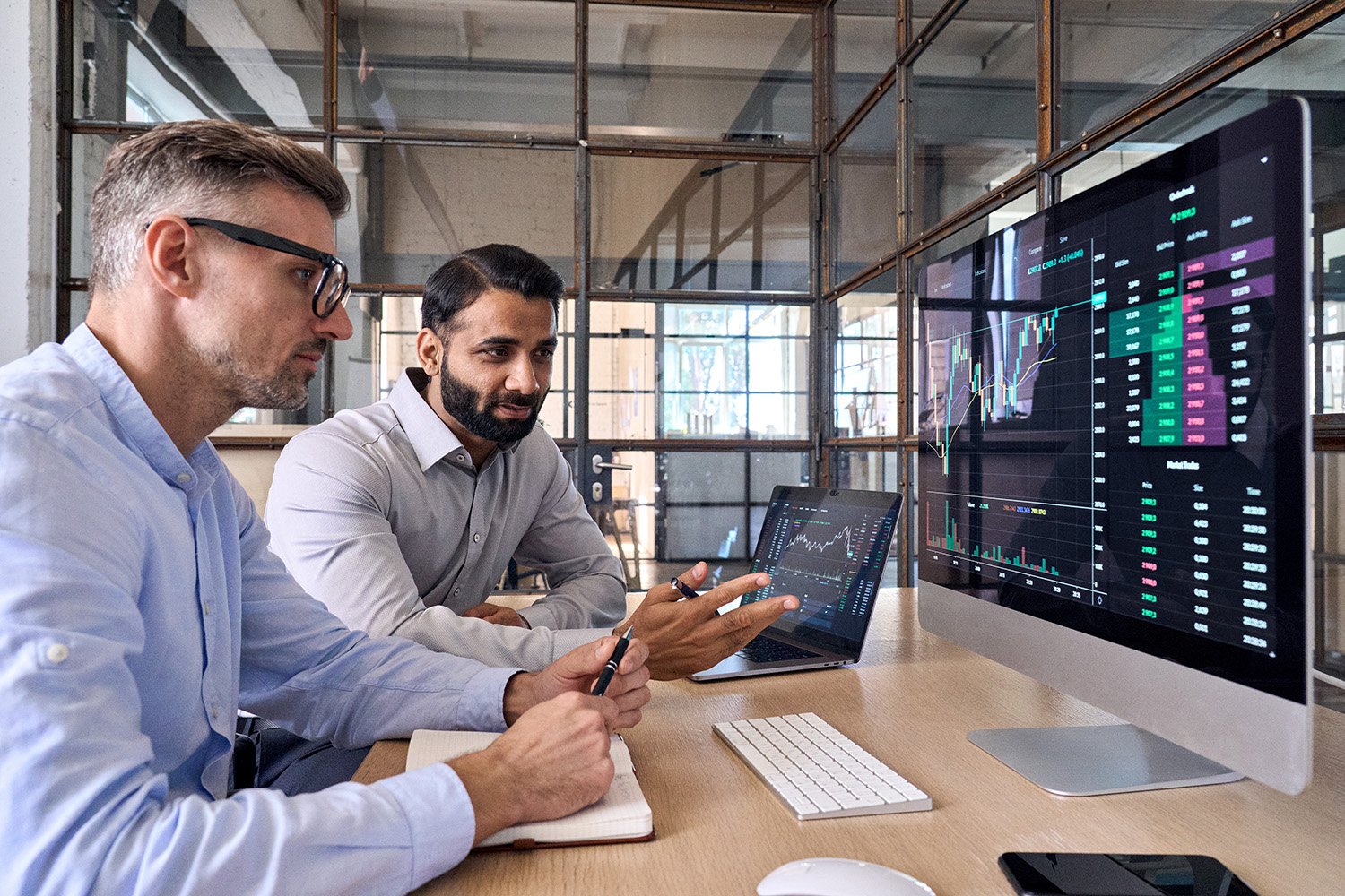 two corporate guys looking at a computer with cryptocurrency information on the screen.