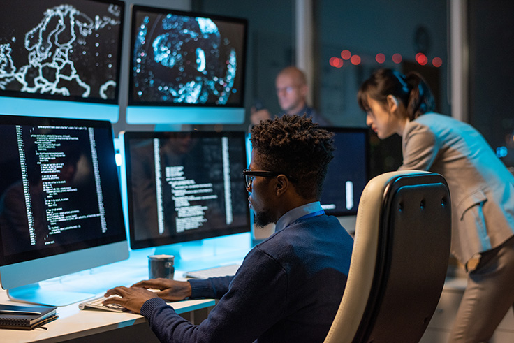 a-man-sitting-at-a-desk-looking-at-six-different-monitors-with-cyber-security-stuff-on-them