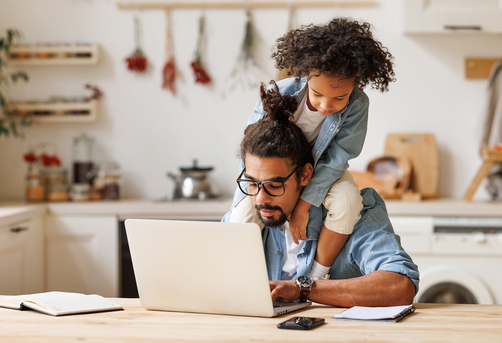 a man working at a computer while a child sits on his shoulders