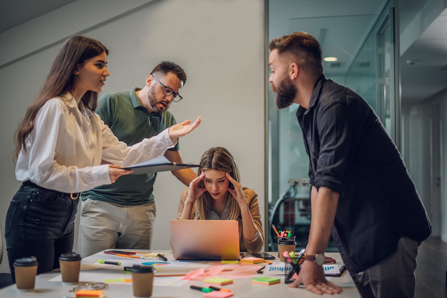 a group of coworkers work on something during a meeting with one of them looking stressed out.
