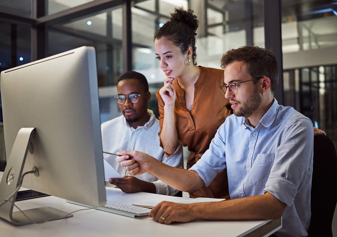a group of coworkers look at a computer together in an office.