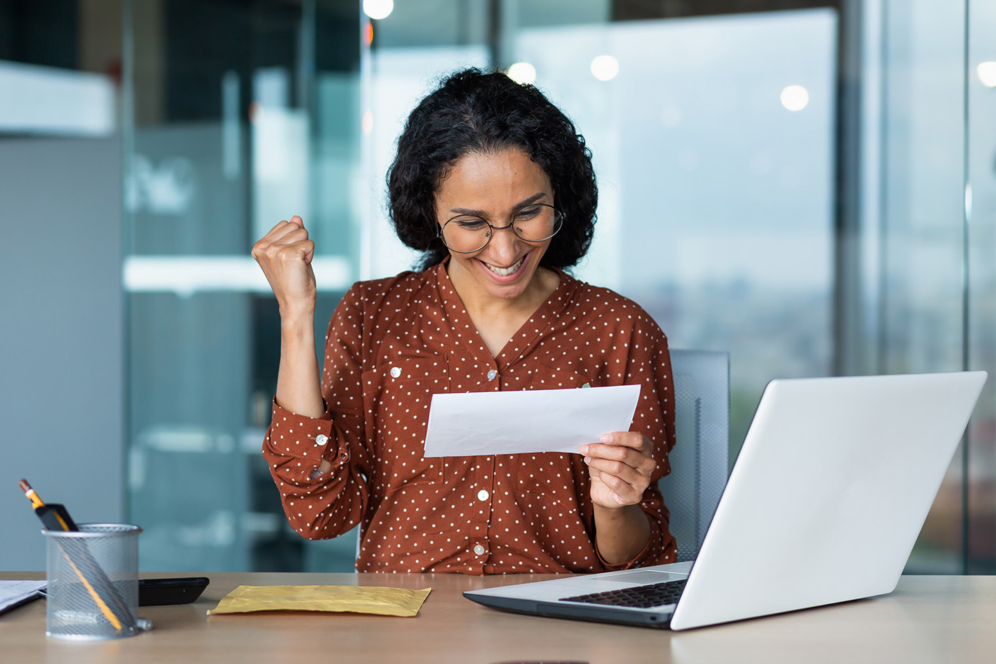 a corporate woman celebrates and smiles when receiving a check at her desk.