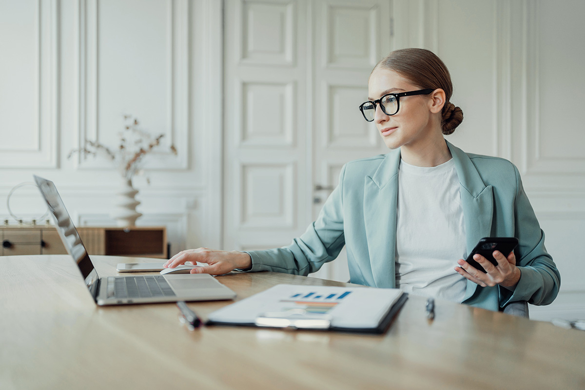 Businesswoman multitasking with laptop and smartphone.