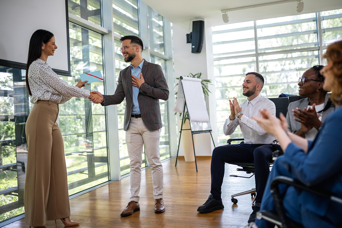 a woman hands a man an envelope during a business meeting while people clap.